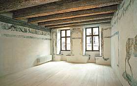 Leerer Raum mit bemalten Wänden, Holzdeckenbalken und zwei großen Fenstern