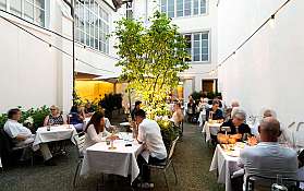 Menschen sitzen an gedeckten Tischen im beleuchteten Innenhof eines Restaurants